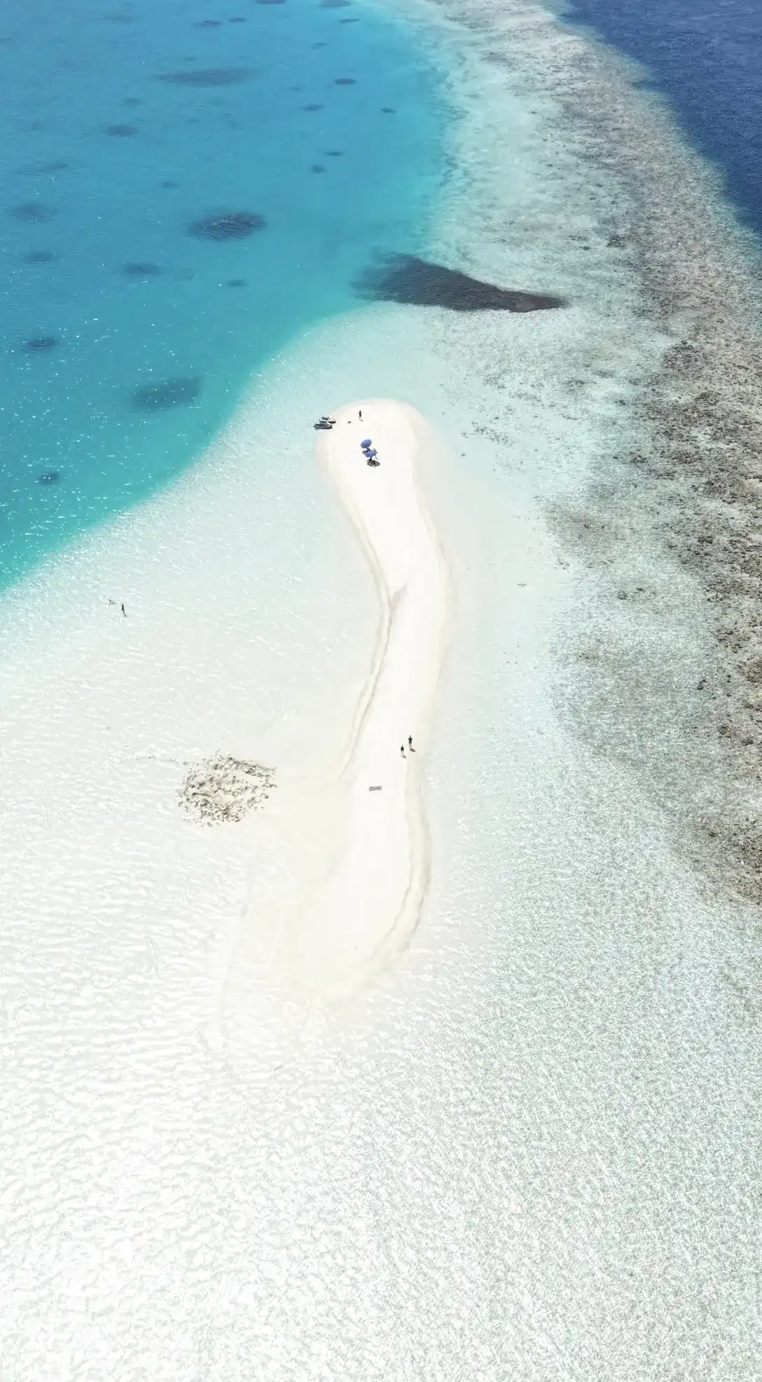 Aerial view of a long white sandbank curving through the lagoon