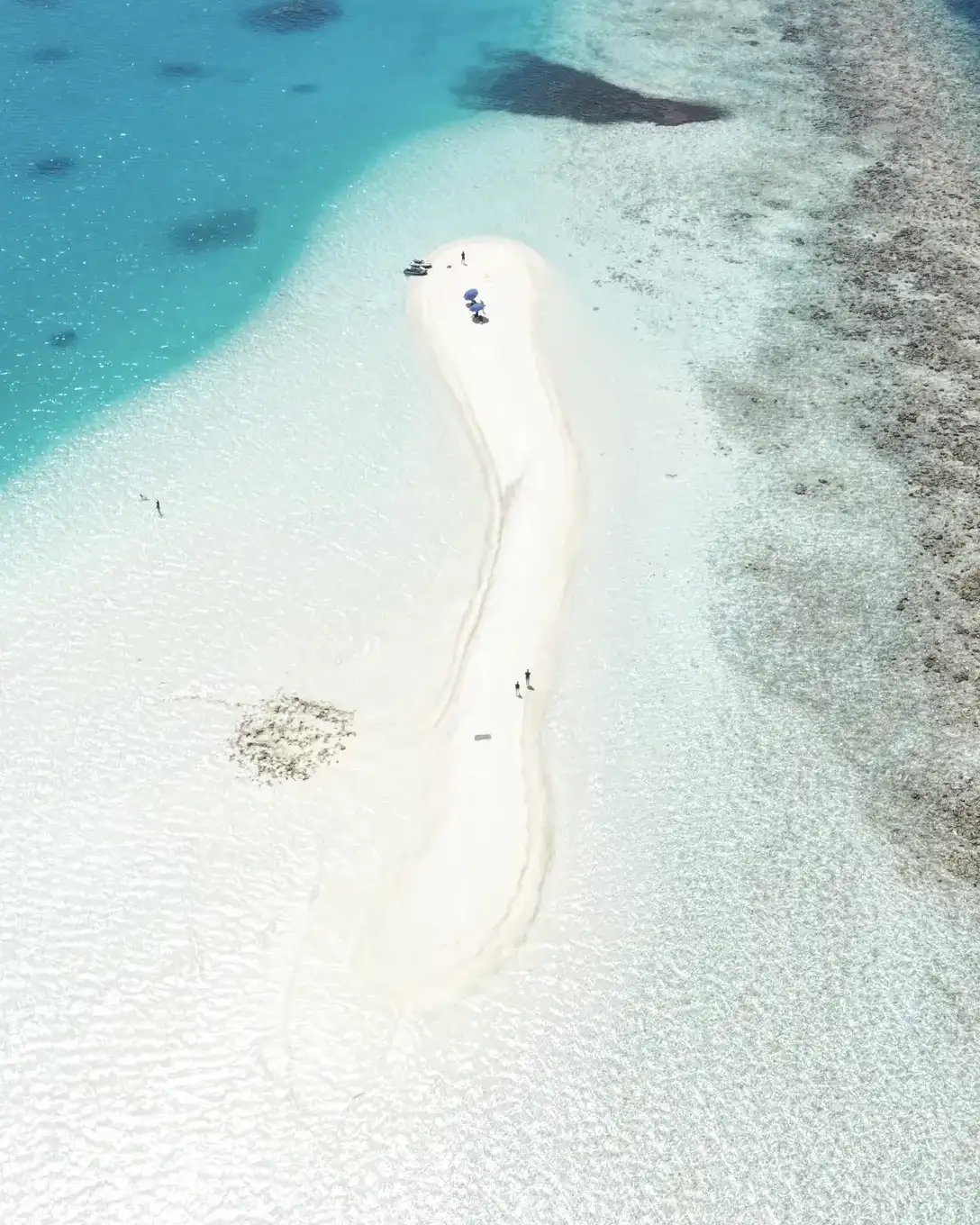 Aerial view of a long white sandbank curving through the lagoon