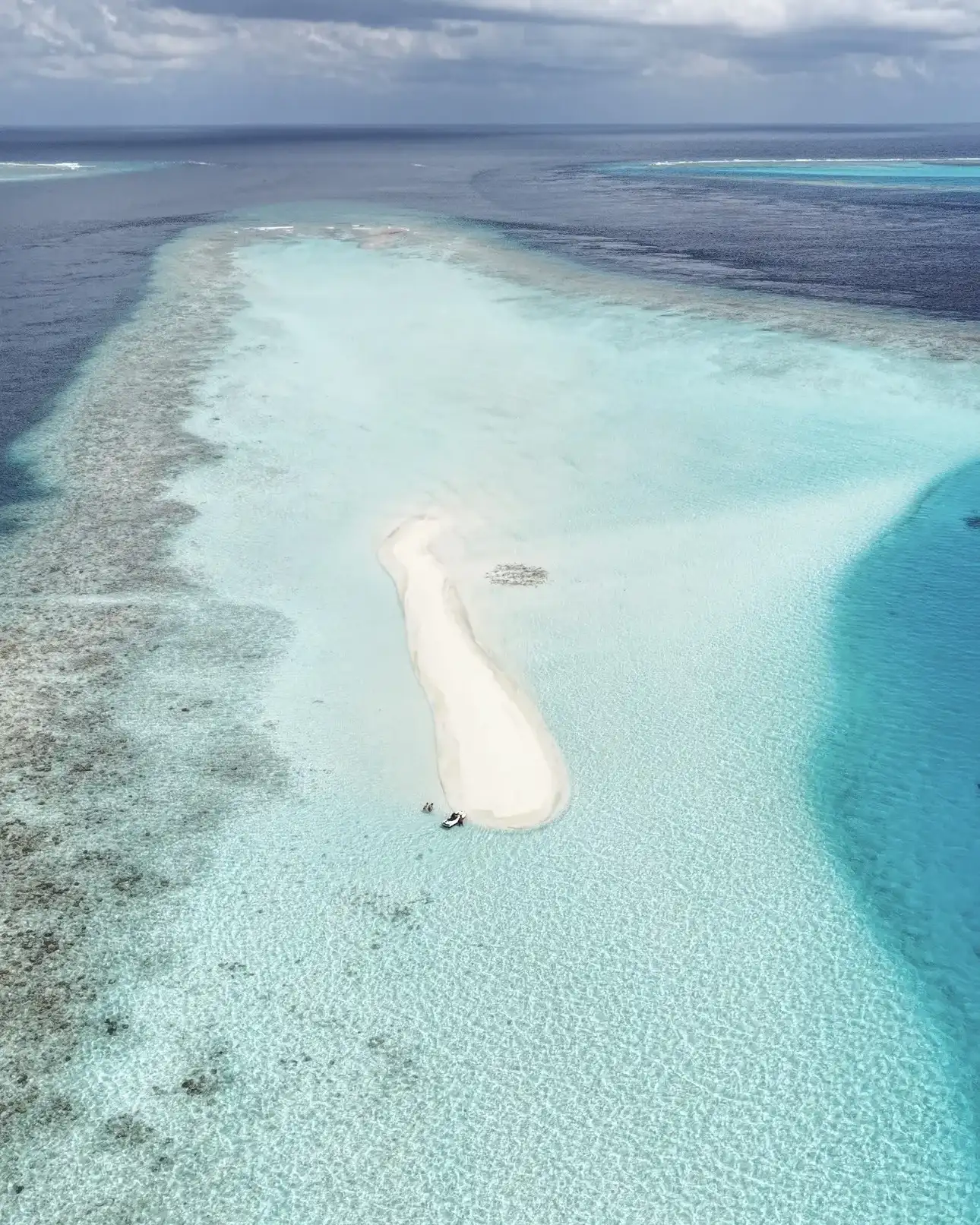 Aerial view of a narrow sandbank surrounded by reef and shallow lagoon
