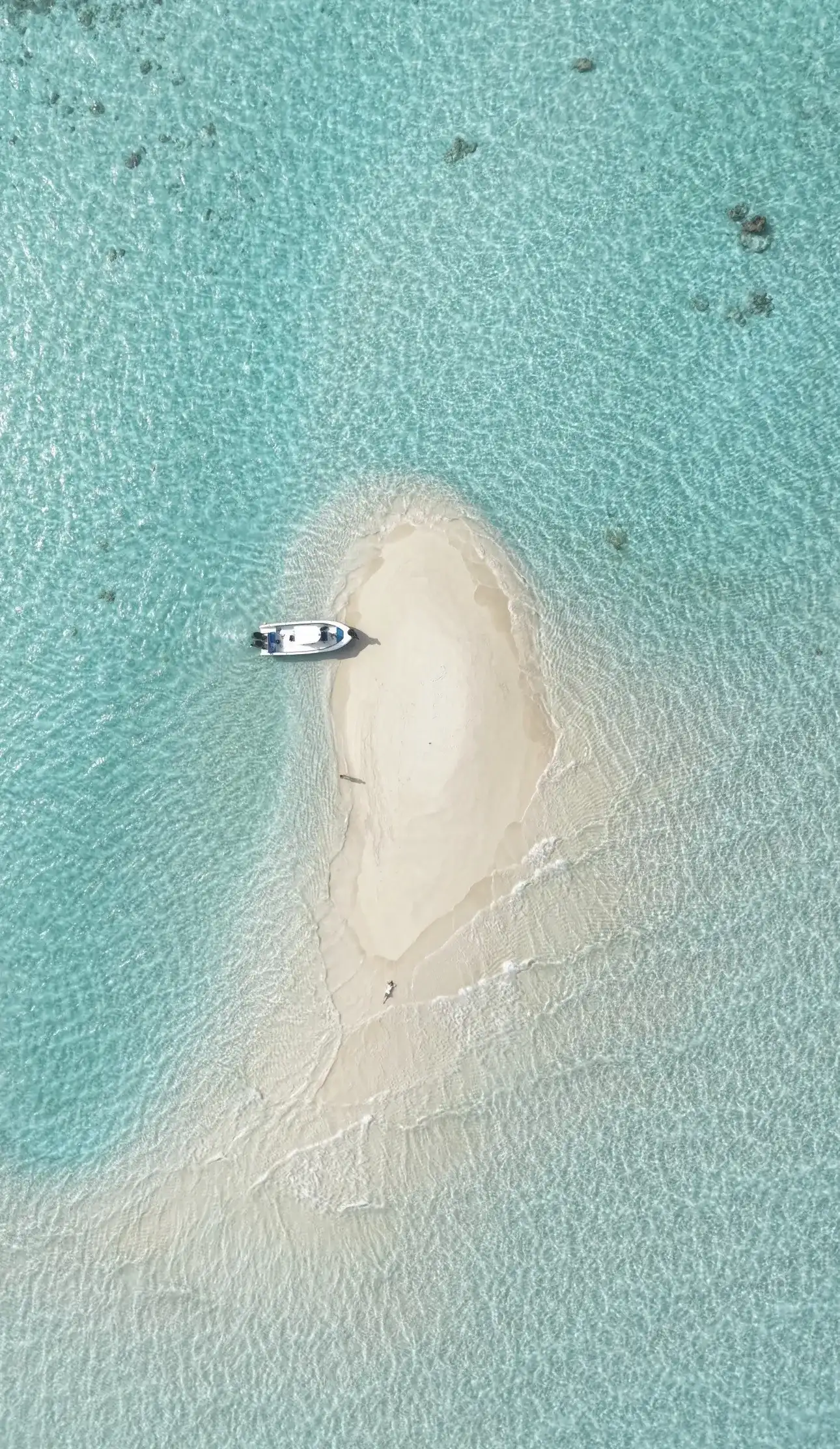 Aerial view of a small round sandbank with a boat moored beside it