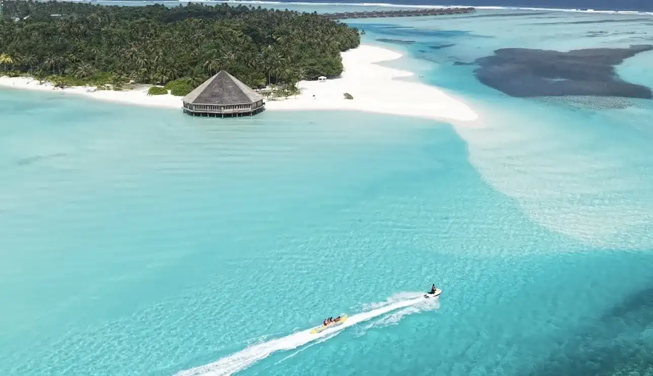 Jet ski crossing a turquoise lagoon past a thatched beach hut