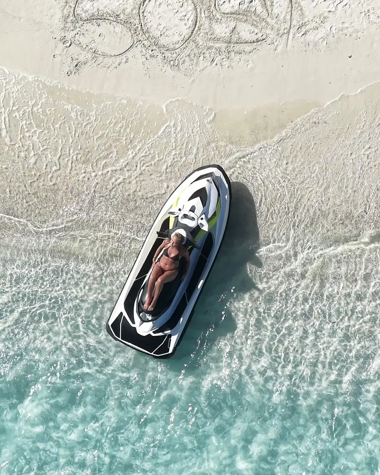 Jet ski pulled up on a white sandbank with a rider resting on it