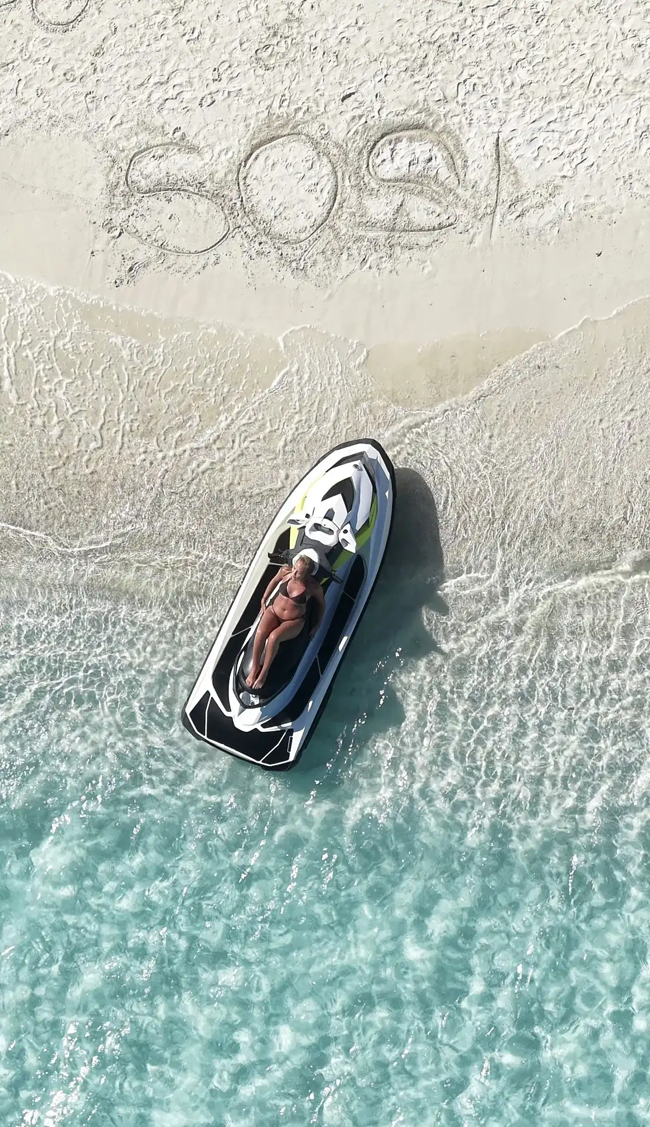 Jet ski pulled up on a white sandbank with a rider resting on it