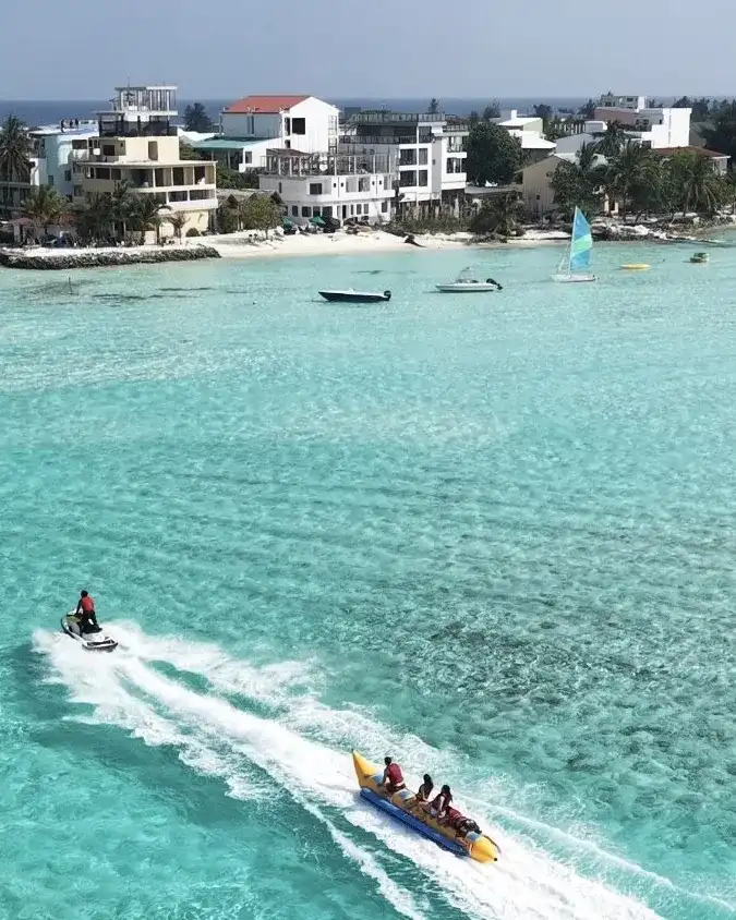 Jet ski towing a yellow banana boat with riders past a local island