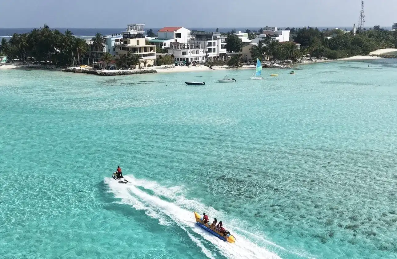 Jet ski towing a yellow banana boat with riders past a local island