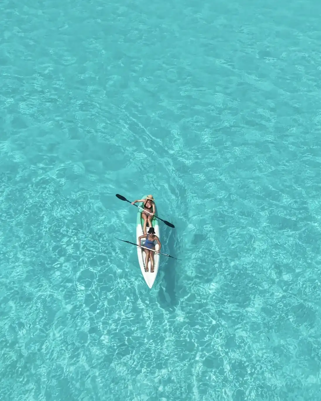 Person paddling a white kayak on clear turquoise water, from above