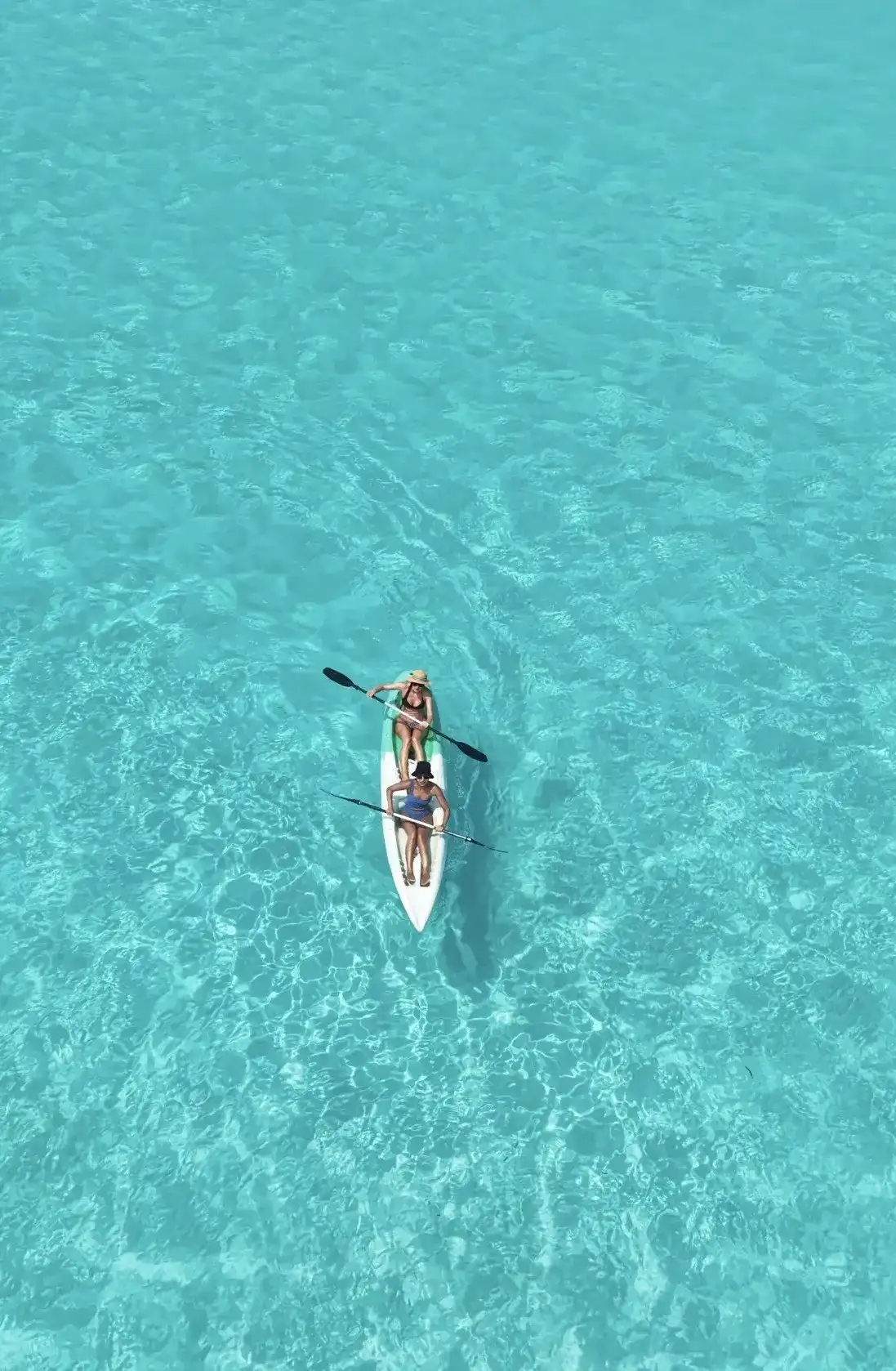 Person paddling a white kayak on clear turquoise water, from above