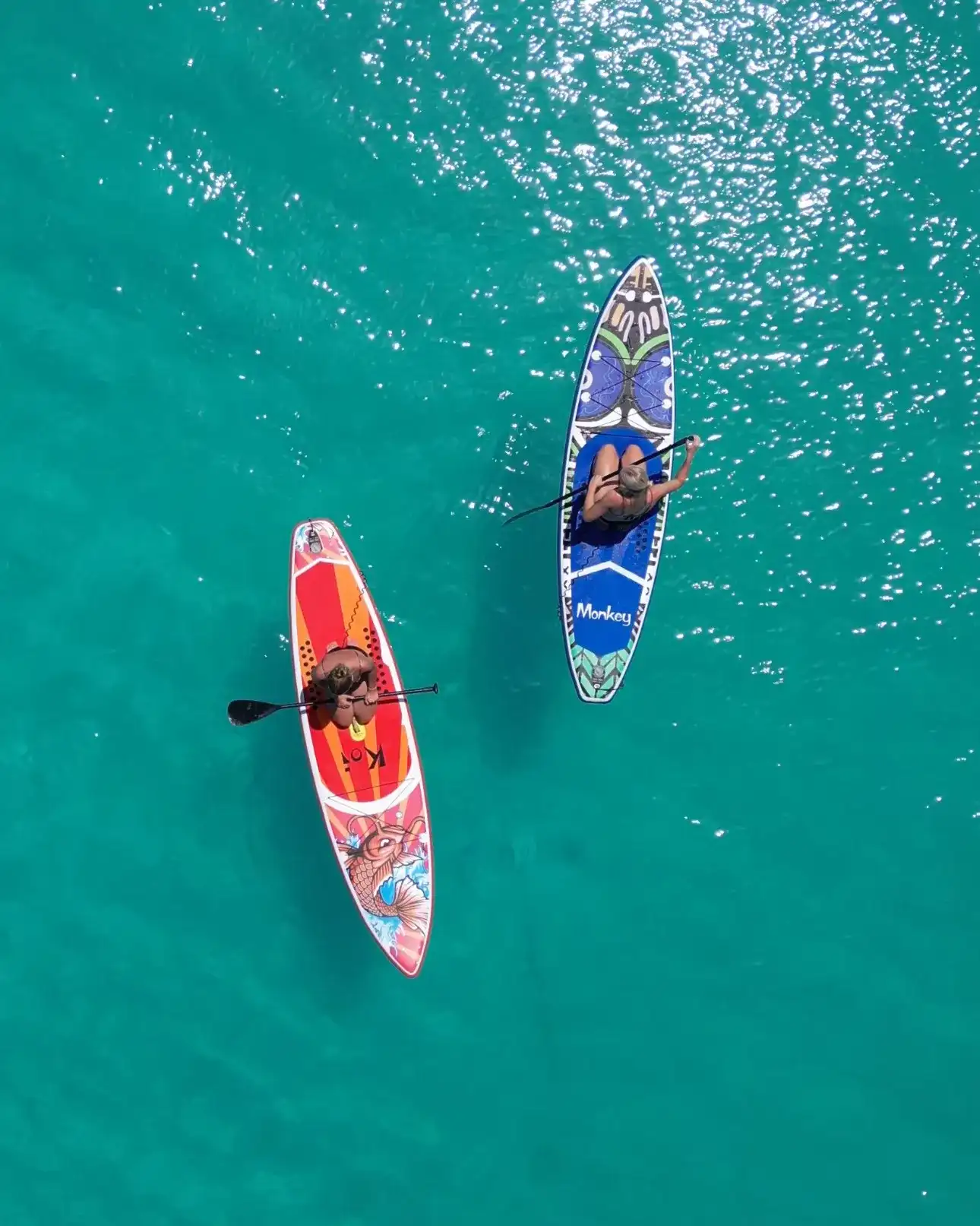 Red and blue kayaks paddling on deep turquoise water, from above