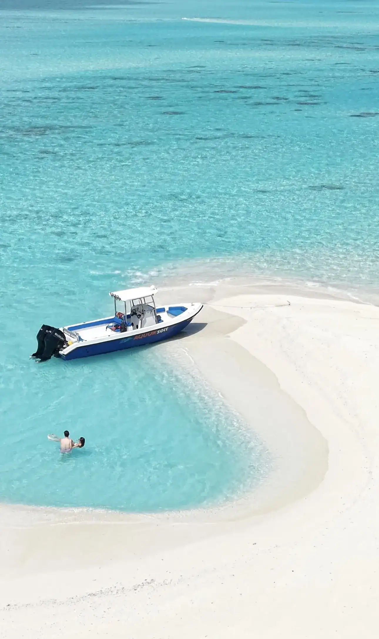 Speedboat pulled up on a white sandbank with a swimmer in the shallows