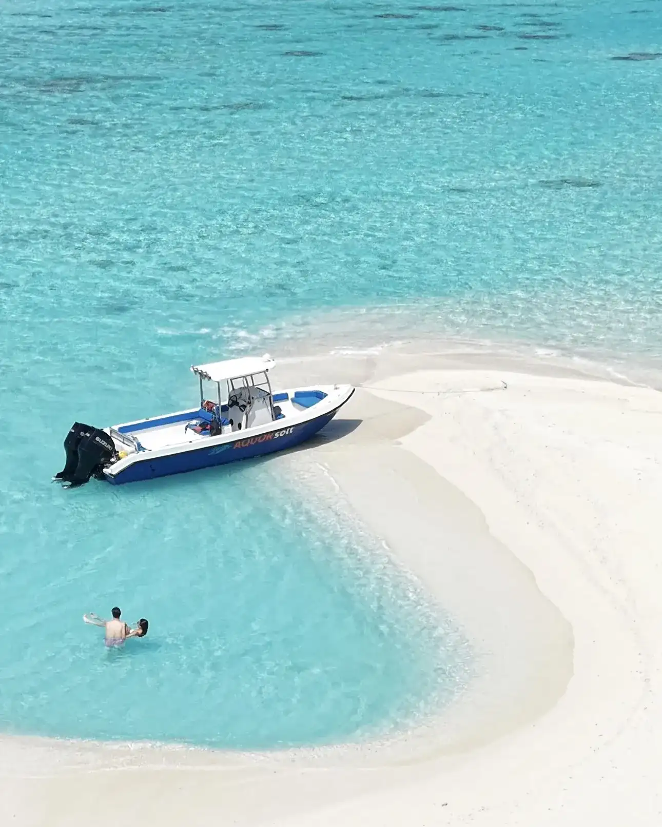 Speedboat pulled up on a white sandbank with a swimmer in the shallows