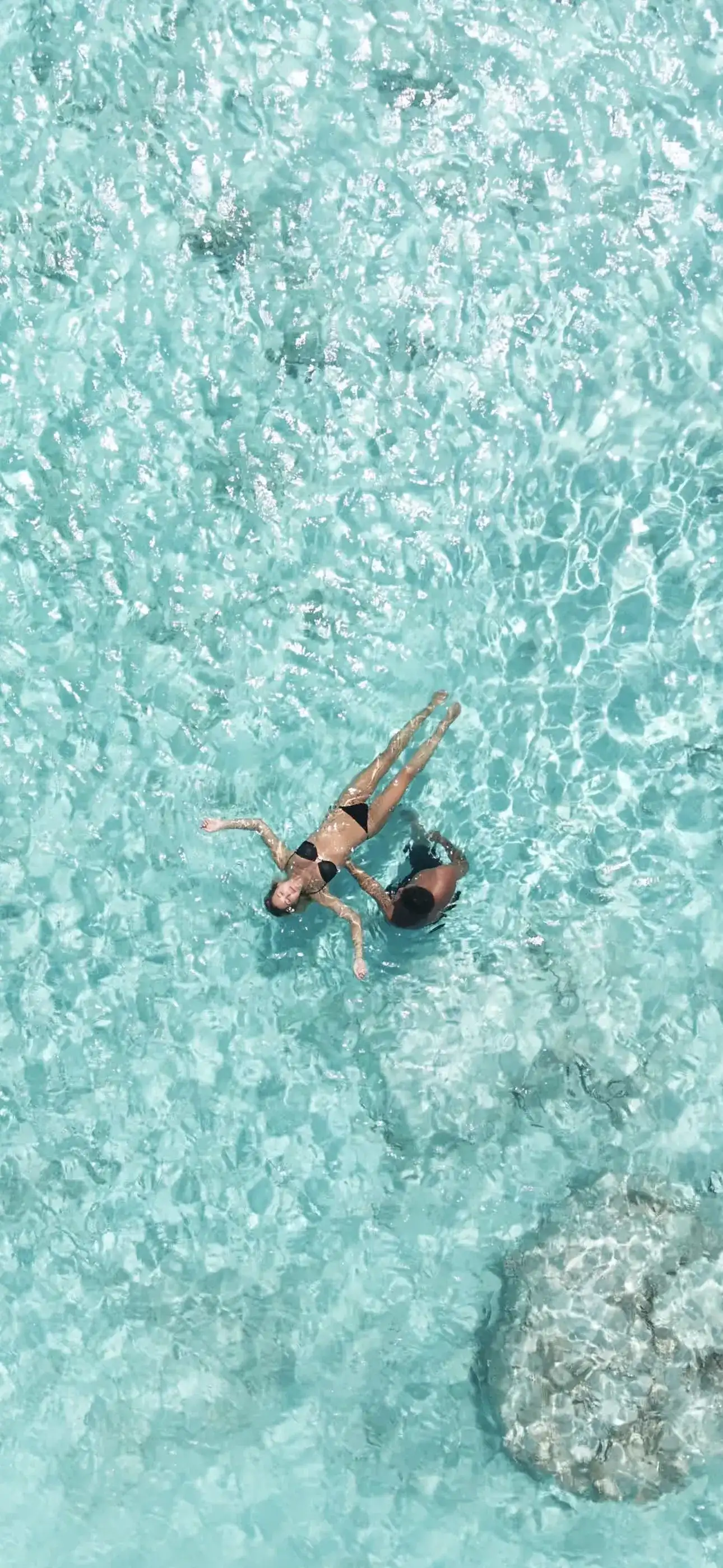 Two people floating in clear turquoise water over a sandy lagoon floor