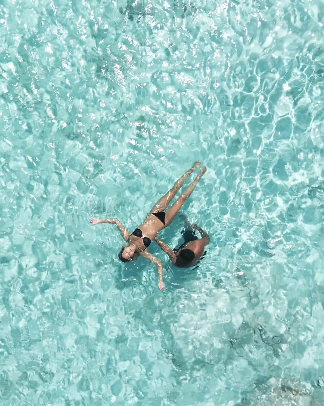 Two people floating in clear turquoise water over a sandy lagoon floor